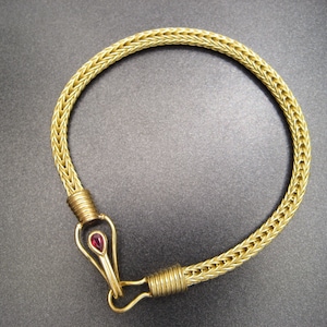 Könnte beinhalten: Ein goldenes Kettenarmband mit einem roten Edelsteinschloss.