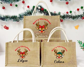 May include: Four beige burlap tote bags with white handles. Each bag features a cartoon reindeer with a red bow or green hat and the words "Merry Christmas." The bags are personalized with names.