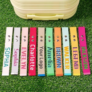 May include: A set of ten rectangular fabric luggage tags in various colors, each featuring two silver metal snaps at the top and a personalized name or text printed vertically in a bold font, including Sophia, Evelyn, Charlotte, Your Logo, Amelia, Brown, Walker, Legend, and Jackson.