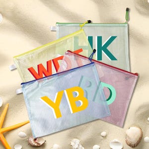 Peut inclure: Plusieurs pochettes zippées en maille de différentes couleurs, chacune affichant de grandes lettres en gras. Les pochettes sont dans des tons de jaune, rouge, vert, bleu et rose. Les lettres sont blanches avec des contours colorés. Le fond est une plage de sable.