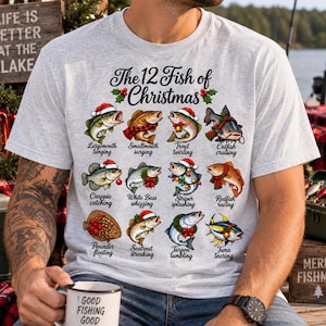 May include: A light gray t-shirt featuring the text The 12 Fish of Christmas and twelve illustrations of fish wearing holiday accessories. Each fish is labeled with a name and action, such as Largemouth lunging, Smallmouth surging, Trout twirling, Catfish cruising, Crappie catching, White Bass whizzing, Striper splashing, Redfish racing, Flounder floating, Seatrout streaking, Tarpon tumbling, and Tuna tearing.