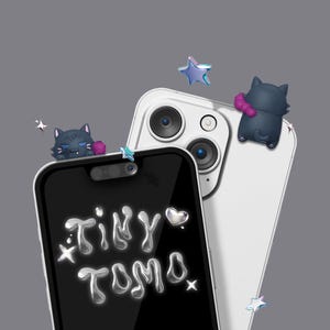 May include: Two smartphones, one black and one white, with decorative cat and star accents. The black phone displays the text "Tiny Tomo" in a silver, bubbly font. The phones are set against a gray background.