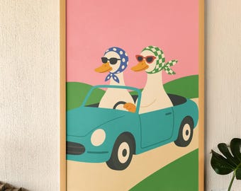 Op de afbeelding: Een ingelijste kunstprint met twee antropomorfe eenden in een turquoise cabriolet. De eenden dragen zonnebrillen en hoofddoeken, een met een blauw stippenpatroon en de andere met een groen ruitpatroon. De achtergrond is roze en groen.