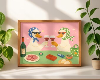 Op de afbeelding: Een ingelijste kunstdruk met twee stripfiguren van ganzen met zonnebrillen en hoofddoeken, die toosten met wijnglazen. De afbeelding bevat een fles wijn, salami en een doosje "Rummy"-kaarten, tegen een roze achtergrond.