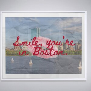 May include: Framed art print featuring a Boston skyline with a red lipstick kiss and the text "Smile, you're in Boston." The image includes sailboats on the water and a cloudy sky.