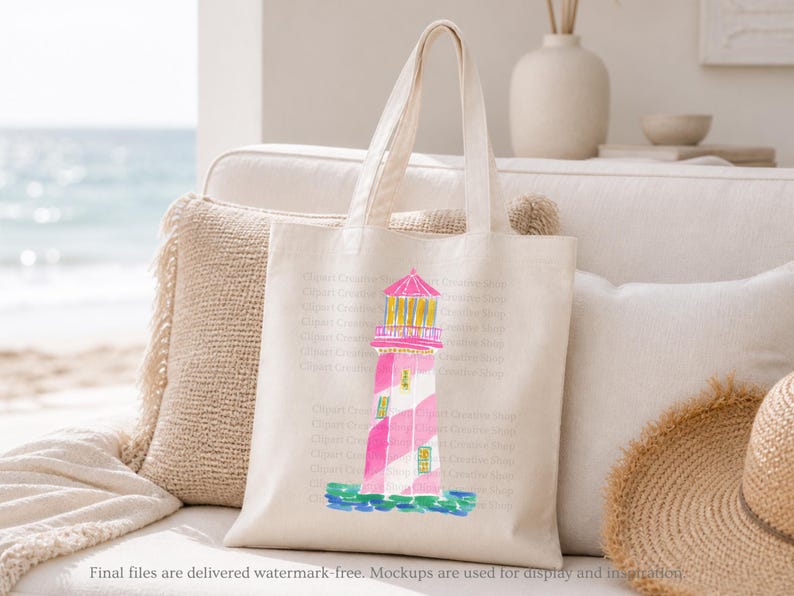 K&ouml;nnte beinhalten: Eine cremefarbene Tragetasche mit einer Aquarellillustration eines rosa und wei&szlig; gestreiften Leuchtturms mit gelben Akzenten. Der Leuchtturm steht auf einem blauen Sockel mit einem rosa Dach. Die Tasche liegt auf einem wei&szlig;en Sofa.