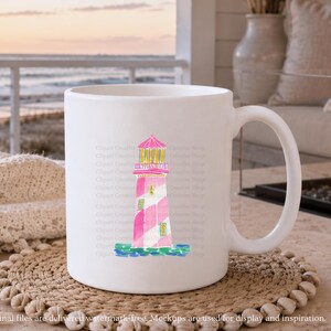 K&ouml;nnte beinhalten: Wei&szlig;e Keramiktasse mit einer Aquarellillustration eines rosa und wei&szlig; gestreiften Leuchtturms, rosa Dach und gelben Akzenten. Die Tasse steht auf einem gewebten Untersetzer. Der Hintergrund zeigt eine Strandszene.