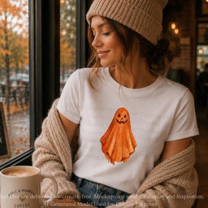 Puede incluir: Una camiseta blanca de manga corta con una ilustraci&oacute;n central estilo acuarela de un fantasma naranja con una cara de calabaza tallada. El fantasma tiene una apariencia drapeada y fluida con texturas de pinceladas visibles en tonos naranja.