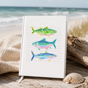 May include: A white notebook with a bookmark displays three colorful watercolor fish illustrations. The fish are green, blue, and blue with pink and yellow accents. The notebook is on a wooden surface near the ocean.