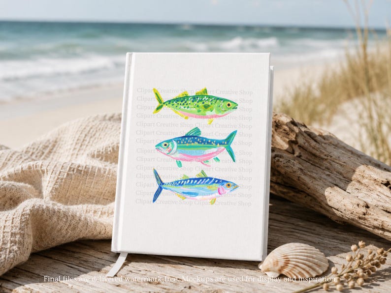 May include: A white notebook with a bookmark displays three colorful watercolor fish illustrations. The fish are green, blue, and blue with pink and yellow accents. The notebook is on a wooden surface near the ocean.