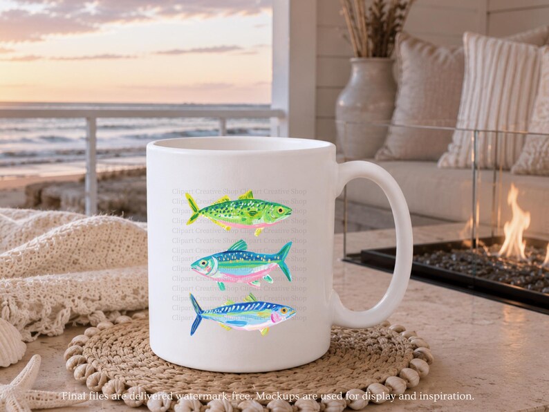 May include: White ceramic mug featuring three colorful watercolor fish illustrations. The fish are in shades of green, blue, pink, and yellow. The mug is on a woven coaster, with a beach scene in the background. The mug has a curved handle.