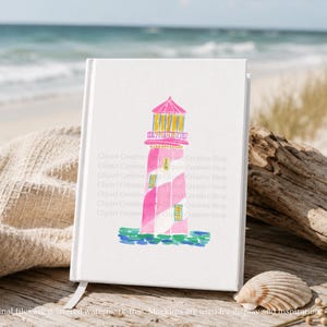 K&ouml;nnte beinhalten: Ein wei&szlig;es Notizbuch mit einer Aquarellillustration eines rosa und wei&szlig;en Leuchtturms. Der Leuchtturm hat eine gelbe Spitze und steht auf einer blau-gr&uuml;nen Basis. Der Hintergrund zeigt einen Strand und das Meer.