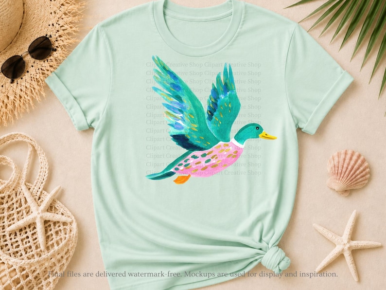 Op de afbeelding: Een licht mintgroen T-shirt met korte mouwen en een centrale afbeelding van een vliegende eend. De eend is afgebeeld met levendige blauwgroene vleugels, een roze lichaam met groene stippen en een gele snavel in een aquarelachtige stijl.