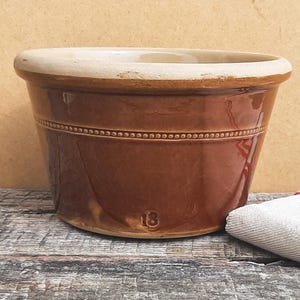 May include: A brown glazed ceramic bowl with a wide, light-coloured rim and a decorative beaded band encircling the upper section. The number 18 is embossed near the base of the bowl, which features a smooth, glossy finish and a tapered shape.
