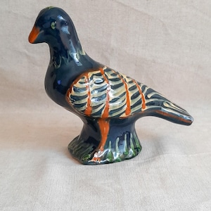 May include: A ceramic bird figurine featuring a glossy dark blue glaze. The wings are decorated with a pattern of cream-colored stripes separated by vibrant orange lines. The base of the bird is accented with green details, and the beak is orange.