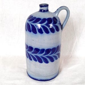 May include: A ceramic jug with a light blue base and dark blue leaf pattern. The jug has a handle and a small spout. The design features a band of leaves around the middle and on the top of the jug.