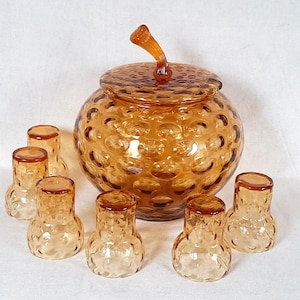 Peut inclure: Un ensemble de service à punch en verre ambré vintage. L'ensemble comprend un saladier rond avec un couvercle et une poignée, et six petits verres. Le verre présente un motif texturé en forme de bulles.