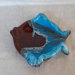 Peut inclure: Un plat en verre en forme de poisson avec un corps brun foncé lisse et des nageoires ainsi qu'une queue bleu turquoise vif. Les bords des sections bleues présentent des détails blancs texturés imitant l'aspect des vagues déferlantes.