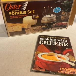 May include: A vintage Oster electric fondue set box with a white and red design. The box features a picture of a fondue pot with cheese and bread. The text on the box reads "Oster electric Fondue Set with thermostatically controlled heat".
