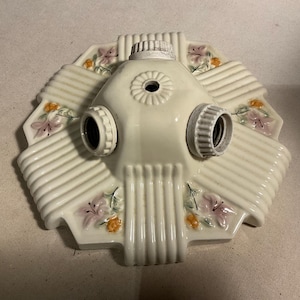 Op de afbeelding: Een witte keramische plafondlamp met drie fittingen en bloemmotieven. De lamp heeft een gegolfde rand en een centraal gat voor montage.