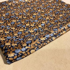 May include: A folded piece of fabric with a blue background and a floral pattern in shades of brown and cream.