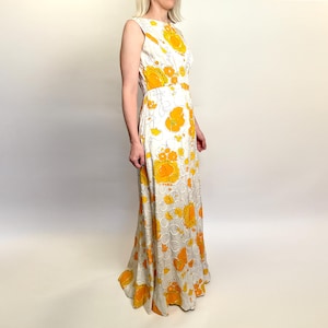 May include: A sleeveless, floor-length dress featuring a white background with a repeating pattern of large, vibrant yellow flowers. The dress has a fitted bodice and a flowing skirt, creating an elegant silhouette. The floral print adds a touch of vintage charm.