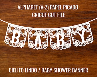 May include: White paper banner spelling "BABY" with floral cut-out designs, strung on a white string. The banner is set against a dark wood background. Text at the top reads "ALPHABET (A-Z) PAPEL PICADO CRICUT CUT FILE".