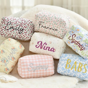 Può includere: Una collezione di trousse personalizzate con vari motivi floreali e colori. Ogni trousse presenta nomi ricamati: "Emily", "Frannie", "Sydney", "Nina" e "BABS". Le trousse sono rettangolari con chiusura a cerniera.