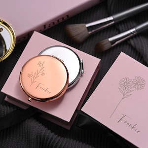 May include: Two pink boxes with a floral design and the name Frankie engraved on them. The boxes contain a compact mirror with a floral design and the name Frankie engraved on it.