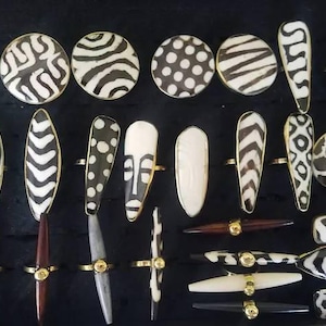 Peut inclure: Une collection de bagues et d'épingles décoratives avec des motifs noirs et blancs, notamment des rayures zébrées, des pois et des motifs abstraits. Les bagues ont des bandes dorées. Les épingles ont des accents dorés et des tiges marron foncé, grises et blanches.