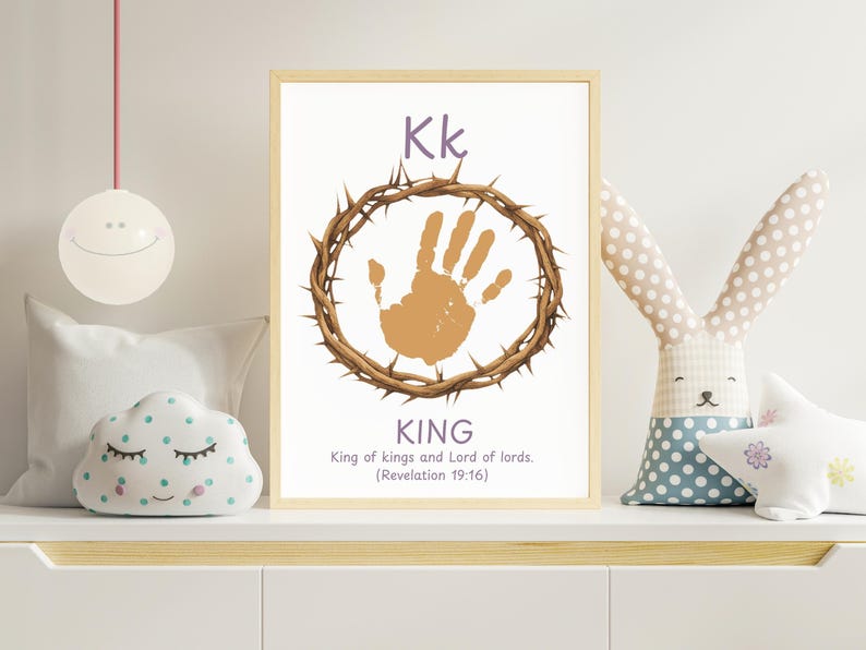 May include: A framed print with the letter "Kk" in purple, a handprint within a crown of thorns, and the word "KING" below. The text "King of kings and Lord of lords. (Revelation 19:16)" is also included. The print is displayed on a white shelf with decorative items.