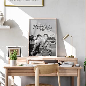 Może przedstawiać: Czarno-biały plakat z tytułem "Rzymskie Wakacje" przedstawiający Audrey Hepburn i Gregory'ego Pecka jadących na skuterze.