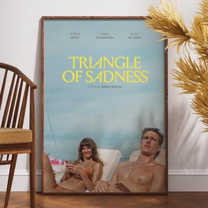 Puede incluir: Un póster de película para la película "Triangle of Sadness", una película de Ruben Östlund. El póster presenta un fondo azul y blanco con el título en texto amarillo. El póster también presenta los nombres de los actores, incluidos Charlbi Dean, Harris Dickinson y Dolly De Leon.
