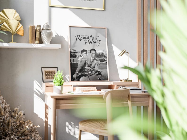 Może przedstawiać: Czarno-biały plakat z tekstem "Roman Holiday" na jasnym drewnianym biurku ze złotą lampą i doniczką z rośliną.