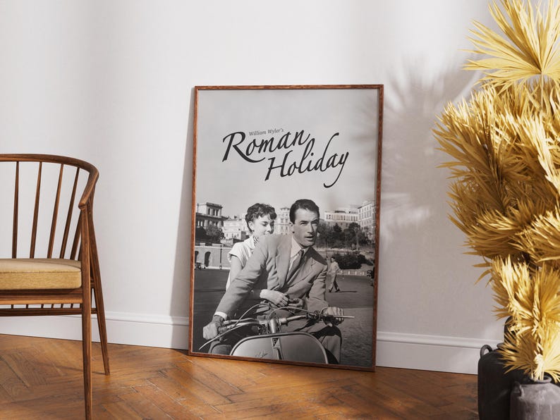 Może przedstawiać: Czarno-biały plakat filmu zatytułowanego "Rzymskie wakacje" z nazwiskiem Williama Wylera u g&oacute;ry. Plakat przedstawia mężczyznę i kobietę jadących skuterem w Rzymie.