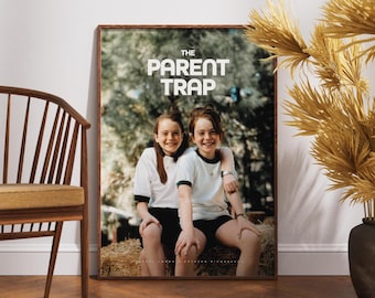 May include: A framed poster featuring the movie title "The Parent Trap" in bold white letters. The image shows two young girls smiling, seated on hay bales. The poster is in a wooden frame, leaning against a white wall.