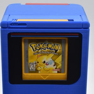以下が含まれることがあります： 青いゲームボーイカートリッジホルダーと黄色のポケモンSpecial Pikachu Editionカートリッジ。ホルダーは長方形のデザインで、黒い画面領域と上部に赤いアクセントがあります。カートリッジは黄色で、ピカチュウのグラフィックが付いています。