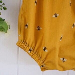 May include: A yellow baby onesie with a bee pattern. The onesie has a gathered elastic waistband.