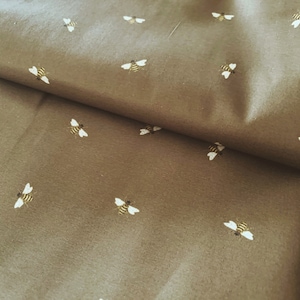 May include: A brown fabric with a repeating pattern of small white bees. The fabric is folded in half, showing the pattern on both sides.