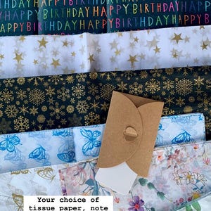 May include: Assortment of gift wrap options including tissue paper with hearts, stars, snowflakes, butterflies, and floral patterns.  A brown envelope is included.  The text reads "Your choice of tissue paper, note card & envelope, and ribbon. Only &pound;2."