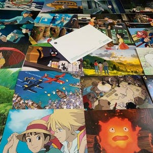 May include: A collection of postcards featuring scenes from Studio Ghibli animated films. The postcards are arranged in a random pattern and include characters like Totoro, Kiki's Delivery Service, and Howl's Moving Castle.