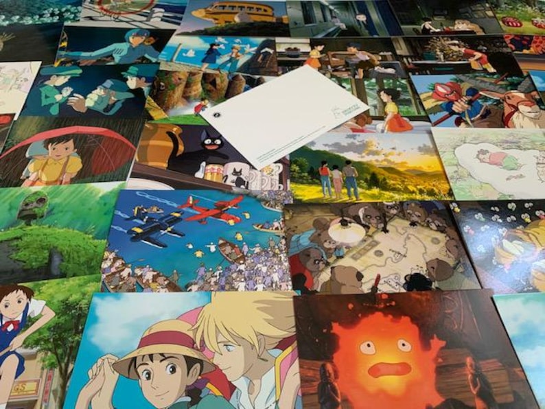 May include: A collection of postcards featuring scenes from Studio Ghibli animated films. The postcards are arranged in a random pattern and include characters like Totoro, Kiki's Delivery Service, and Howl's Moving Castle.