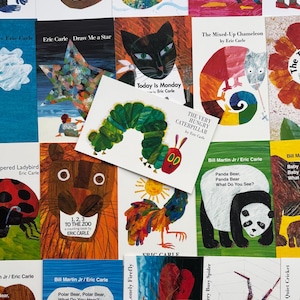 May include: A collection of children's books by Eric Carle, featuring colorful illustrations. Titles include "The Very Hungry Caterpillar," "Today is Monday," and "Draw Me a Star." The books are arranged on a white surface.