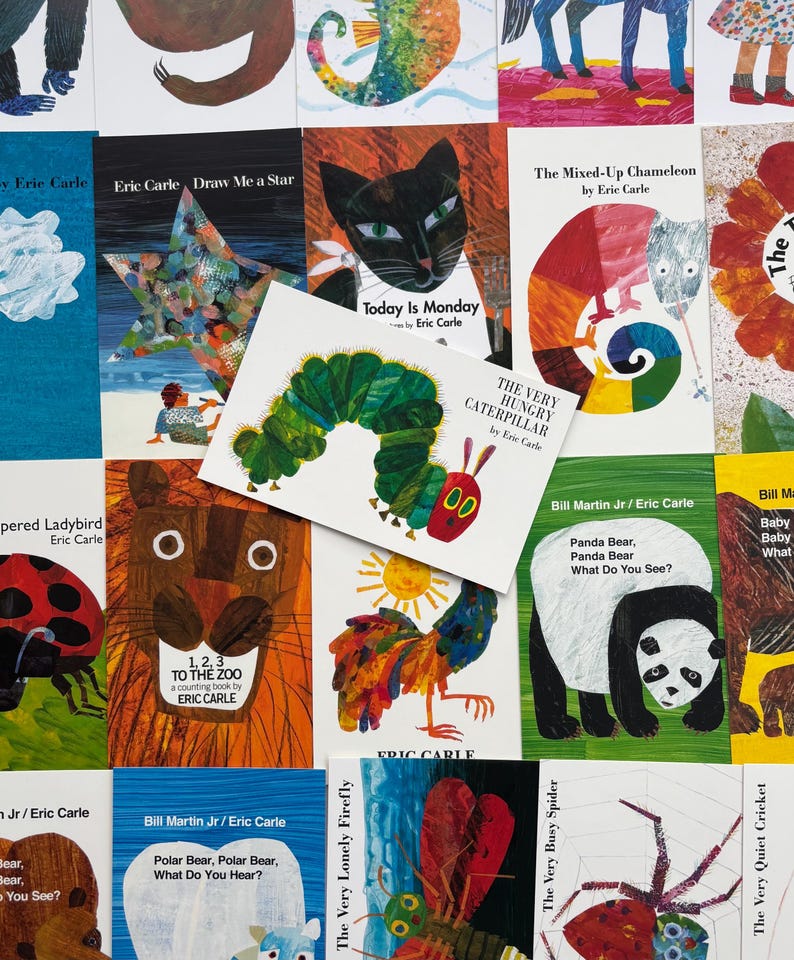 May include: A collection of children's books by Eric Carle, featuring colorful illustrations. Titles include "The Very Hungry Caterpillar," "Today is Monday," and "Draw Me a Star." The books are arranged on a white surface.