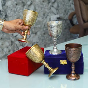 Könnte beinhalten: Vier verzierte Silber- und Kupferkelche mit aufwendigen Designs, präsentiert auf einer blauen Samtbox und einer roten Samtbox.