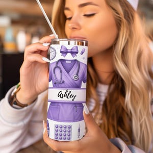 May include: A purple and white stainless steel tumbler with a design of a nurse's uniform, a stethoscope, a syringe, and pills. The name "Ashley" is written on the tumbler.