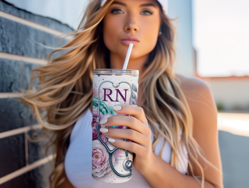 May include: A white stainless steel tumbler with a floral design and a stethoscope. The tumbler has the letters "RN" in purple on the front.