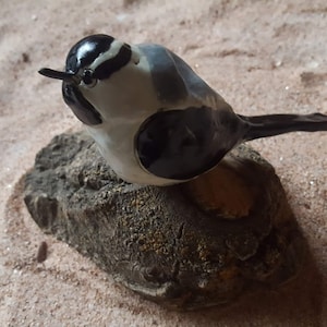 May include: A ceramic bird figurine with black, white, and gray paint. The bird is perched on a small, gray rock.