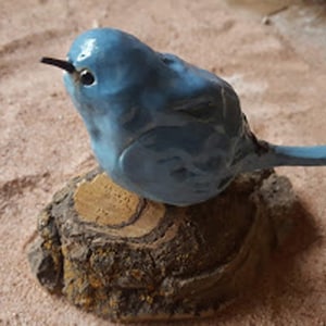 May include: A blue ceramic bird figurine perched on a small, brown, tree stump. The bird has a long, thin beak and a detailed, textured surface.
