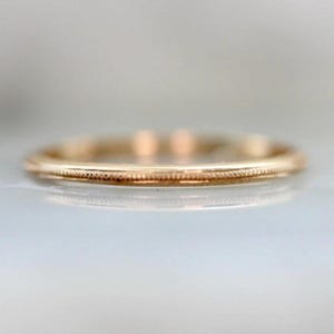 Könnte beinhalten: Nahaufnahme eines goldfarbenen Rings mit einem filigranen Perlendesign um das Band. Der Ring ist schmal und hat eine polierte Oberfläche, die das Licht reflektiert. Der Ring ist wahrscheinlich aus Gold oder einem goldfarbenen Metall.